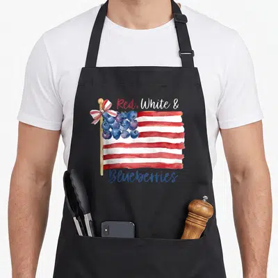 Funny blueberries apron - Watercolor flag with red white stripes and blueberry cluster canton — shown on a black cotton canvas apron against a white background
