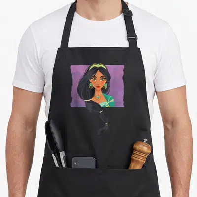 Live princess apron - Cartoon woman portrait with purple background, green top, gold crown, and black braided hair — shown on a black cotton canvas apron against a white background