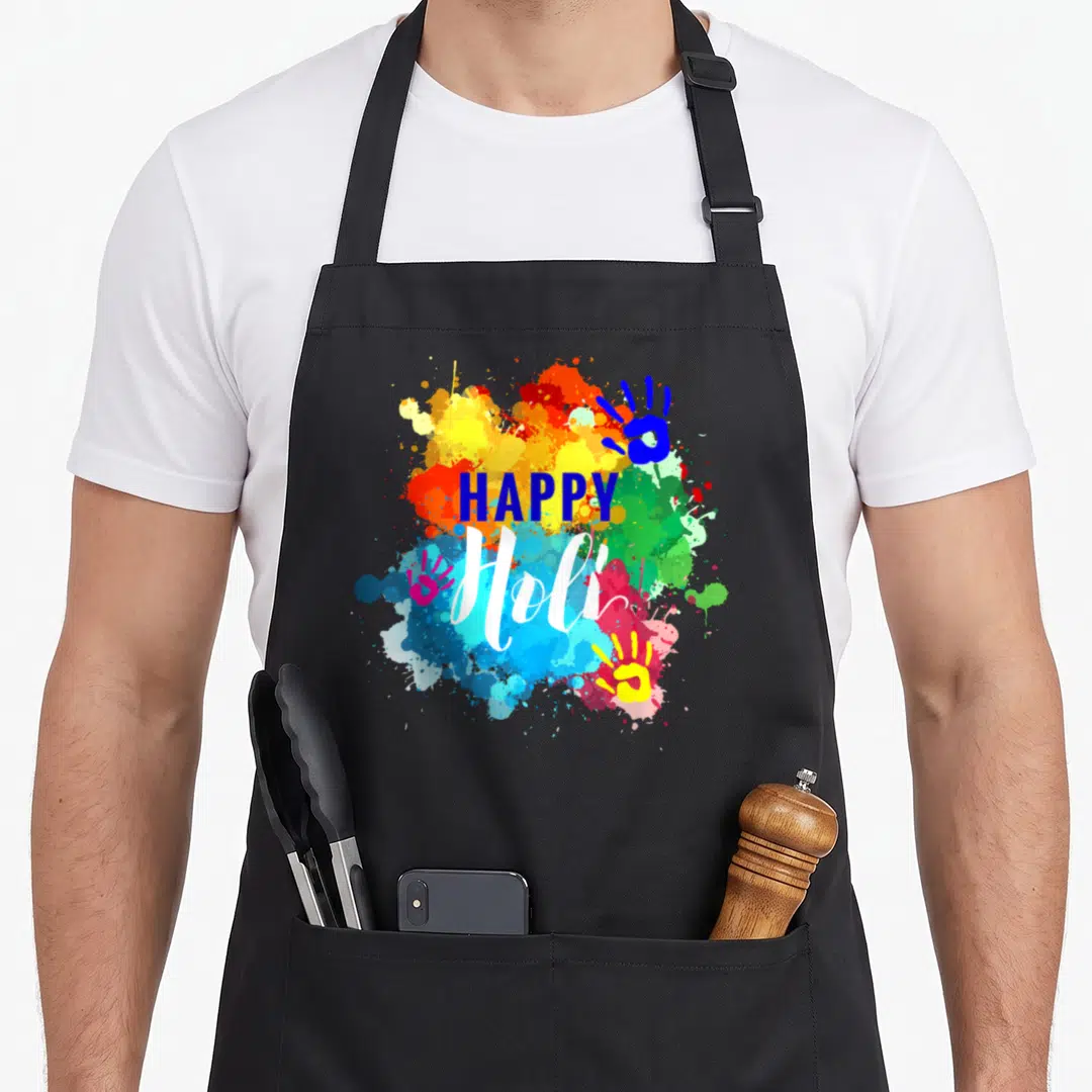 Holi spring apron - HAPPY Holi text over multicolored watercolor splashes with three blue, pink, and yellow handprints — shown on a black cotton canvas apron against a white background