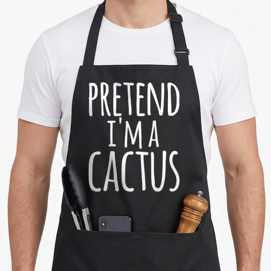 Easy funny halloween aprons - White stacked text reading PRETEND I'M A CACTUS on grey background — shown on a black cotton canvas apron against a white background