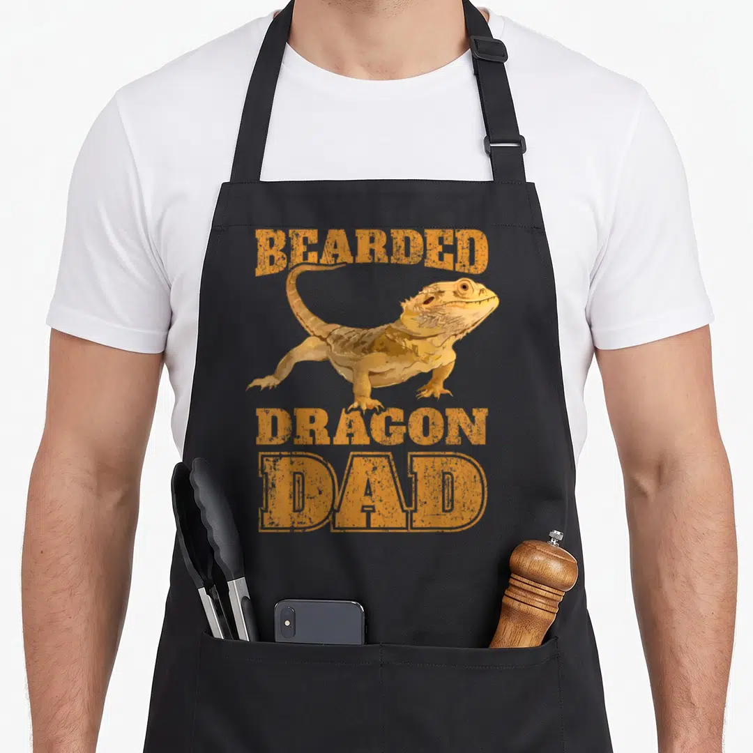 Papa dragon apron - Realistic orange bearded dragon illustration with bold distressed text — shown on a black cotton canvas apron against a white background
