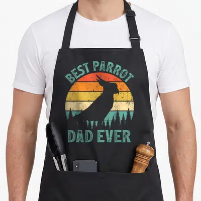 Funny parrot father day apron - Retro parrot silhouette against striped sun with best parrot dad ever text — shown on a black cotton canvas apron against a white background