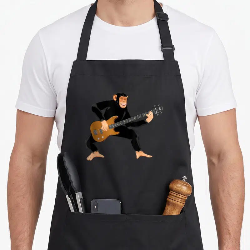 Playing chimpanzee apron - Cartoon chimpanzee standing and playing a brown electric bass guitar in black and tan — shown on a black cotton canvas apron against a white background