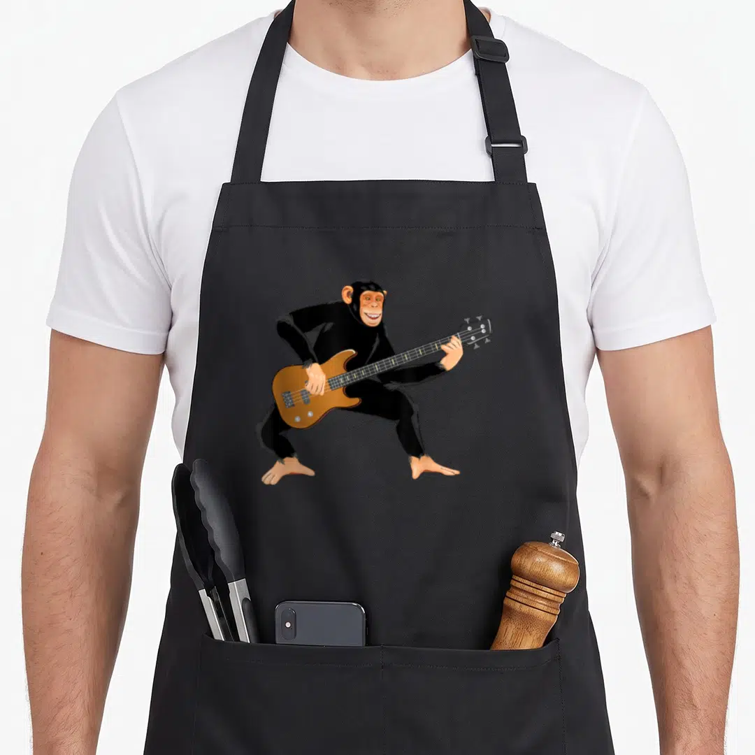 Playing chimpanzee apron - Cartoon chimpanzee standing and playing a brown electric bass guitar in black and tan — shown on a black cotton canvas apron against a white background