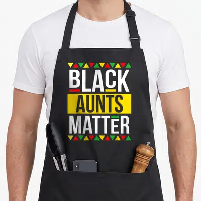 Aunt grandma apron - Black Aunts Matter text with yellow box and colorful triangle borders — shown on a black cotton canvas apron against a white background