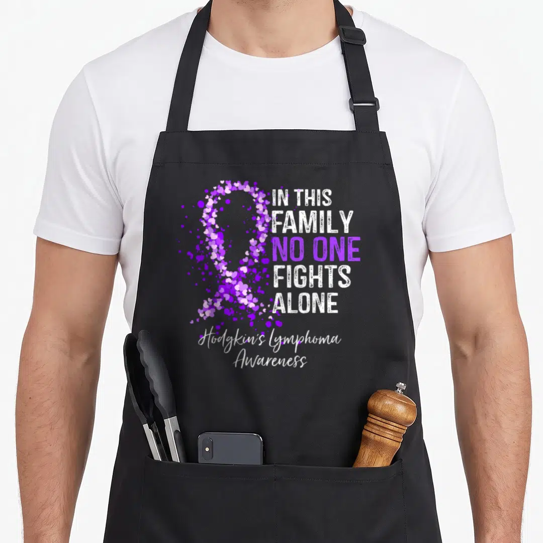 Hodgkin family aprons - Purple heart ribbon and IN THIS FAMILY NO ONE FIGHTS ALONE text for Hodgkin's Lymphoma Awareness — shown on a black cotton canvas apron against a white background
