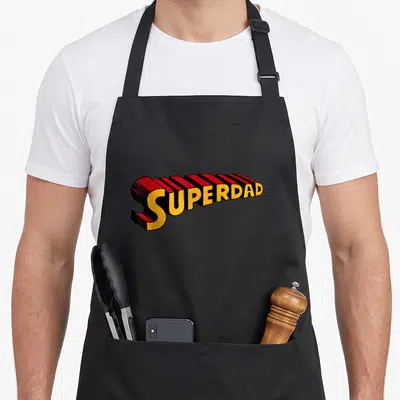 Superdad superhero apron - 3D SUPERDAD text in yellow red and black block letters — shown on a black cotton canvas apron against a white background