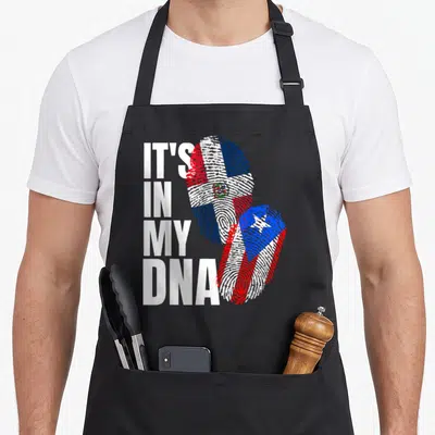 Dominican heritage aprons - IT'S IN MY DNA text next to two fingerprints filled with Dominican and Puerto Rican flags — shown on a black cotton canvas apron against a white background