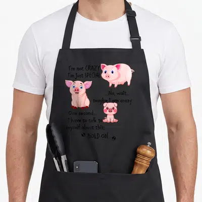 Funny pig special aprons - Three pink cartoon pigs surrounding black text about being special and crazy — shown on a black cotton canvas apron against a white background
