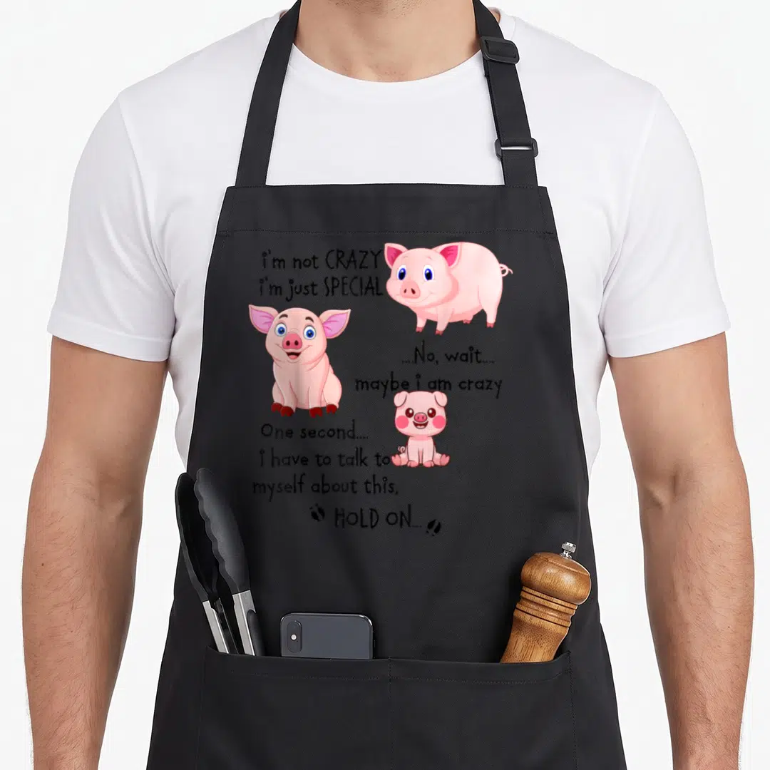 Funny pig special aprons - Three pink cartoon pigs surrounding black text about being special and crazy — shown on a black cotton canvas apron against a white background