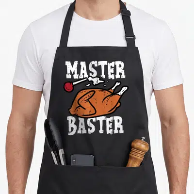 Master thanksgiving day aprons - Master Baster text surrounding cartoon orange turkey with red baster spraying juice — shown on a black cotton canvas apron against a white background