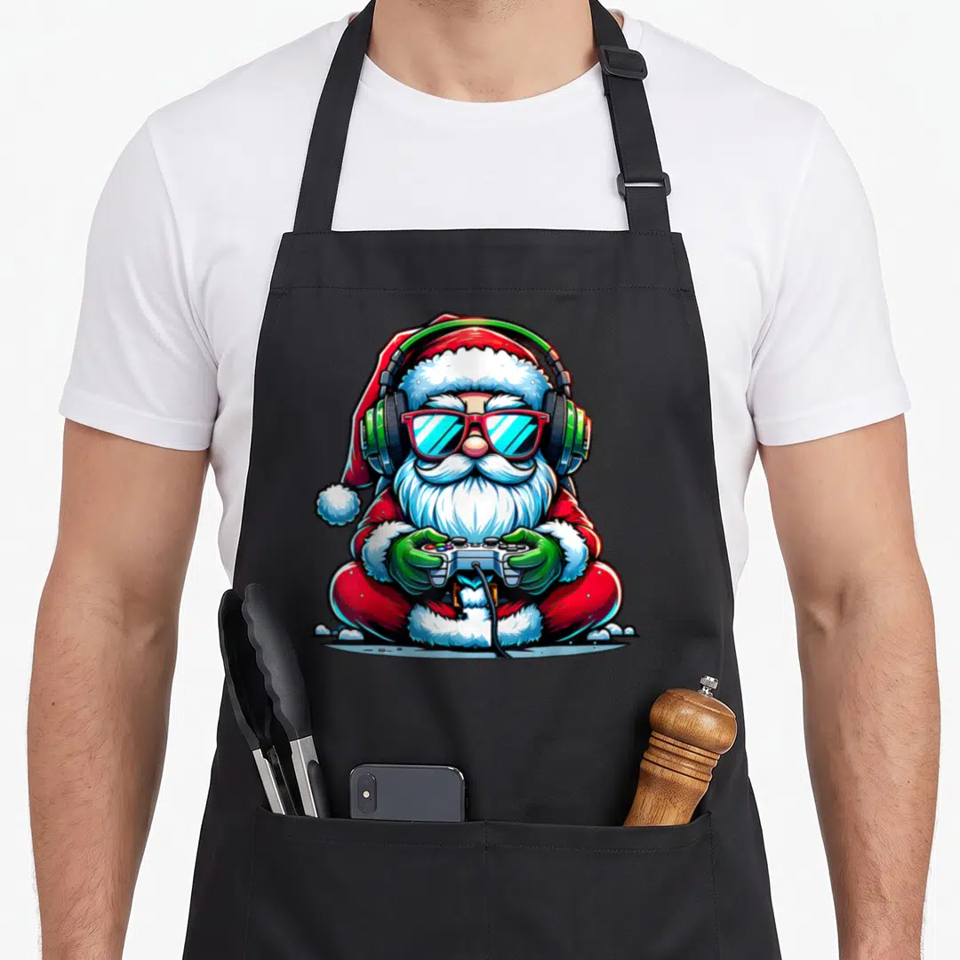 Gamer santa apron - Cartoon Santa sitting cross-legged holding a game controller wearing headphones and sunglasses — shown on a black cotton canvas apron against a white background