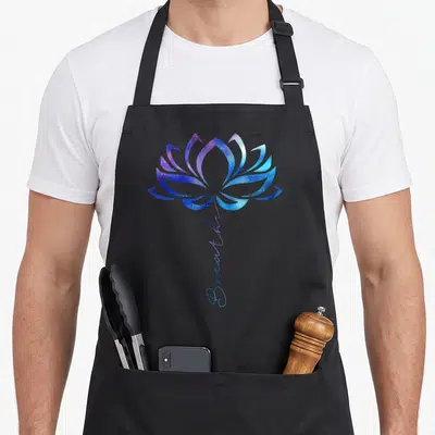 Lotus watercolors apron - Blue and purple lotus flower with vertical cursive Breathe text in galaxy texture — shown on a black cotton canvas apron against a white background
