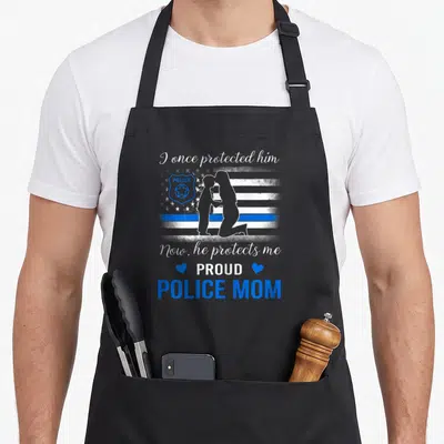 Blue line american flag apron - Distressed white and blue flag with mother son silhouette and proud police mom text — shown on a black cotton canvas apron against a white background