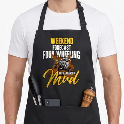 Weekend atv lover apron - Stacked text WEEKEND FORECAST FOUR WHEELING WITH A CHANCE OF Mud around cartoon ATV rider — shown on a black cotton canvas apron against a white background