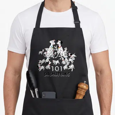 Shot dalmatian apron - Cartoon Dalmatian puppies and adults with 101 DALMATIANS text and colored collars — shown on a black cotton canvas apron against a white background