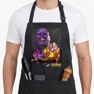 Infinity stained apron - Shattered purple and gold Thanos mosaic with Avengers Infinity War logo — shown on a black cotton canvas apron against a white background