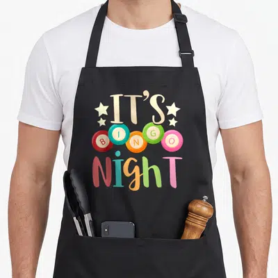 Gambling bingo apron - IT'S BINGO Night text with five red blue orange green and pink bingo balls and stars — shown on a black cotton canvas apron against a white background