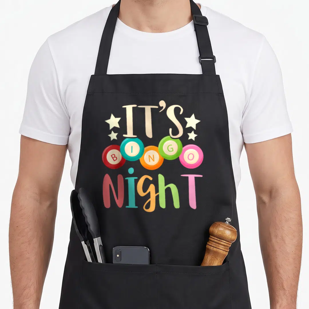 Gambling bingo apron - IT'S BINGO Night text with five red blue orange green and pink bingo balls and stars — shown on a black cotton canvas apron against a white background
