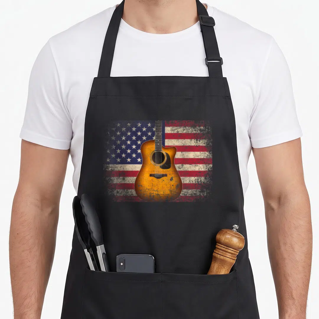 Guitar cook's country aprons - Acoustic guitar centered on distressed USA flag with orange and blue tones — shown on a black cotton canvas apron against a white background