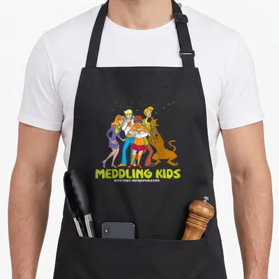 Meddling have better apron - Five cartoon characters holding a book with grey monster silhouettes and yellow stacked — shown on a black cotton canvas apron against a white background