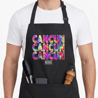 Summer spring aprons - Tie-dye CANCUN text repeated three times above MEXICO in pink blue yellow white — shown on a black cotton canvas apron against a white background