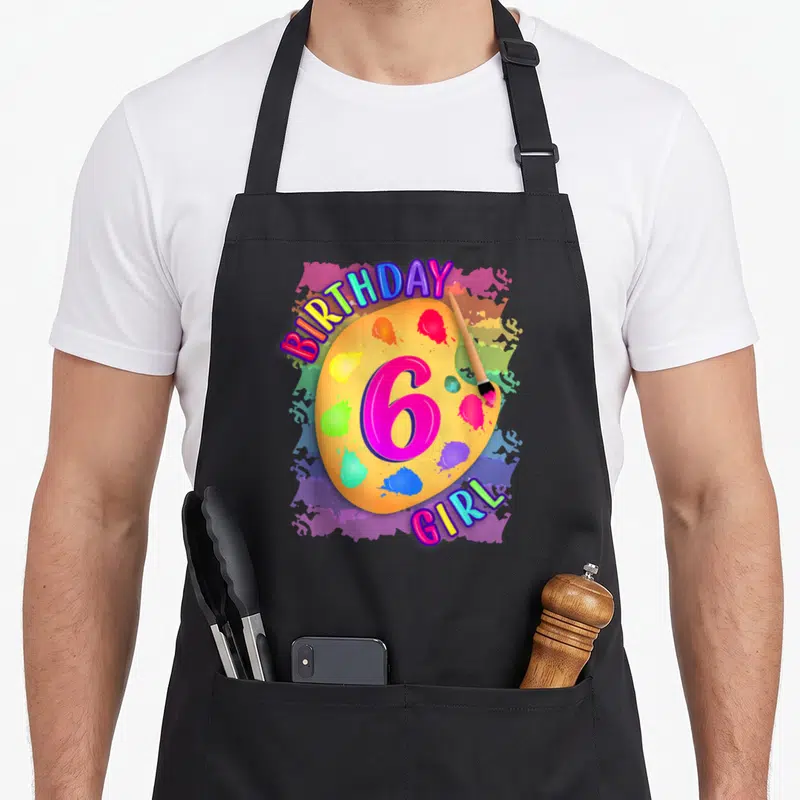Painting 6th birthday apron - BIRTHDAY 6 GIRL text over yellow palette with paintbrush and colorful splatters — shown on a black cotton canvas apron against a white background