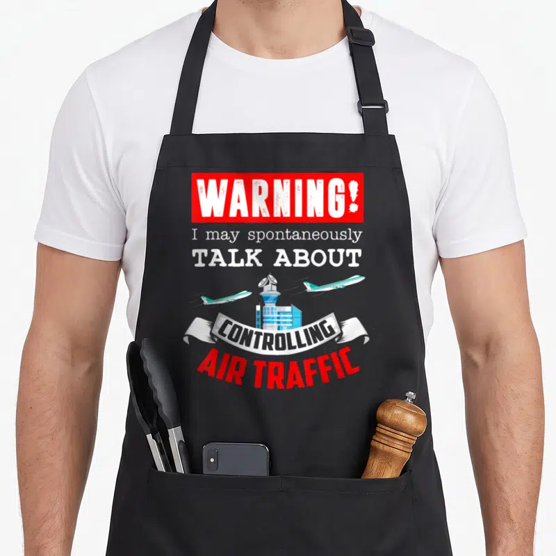 Air joke apron - Warning sign and air traffic control tower with two airplanes in red white and blue cartoon style — shown on a black cotton canvas apron against a white background