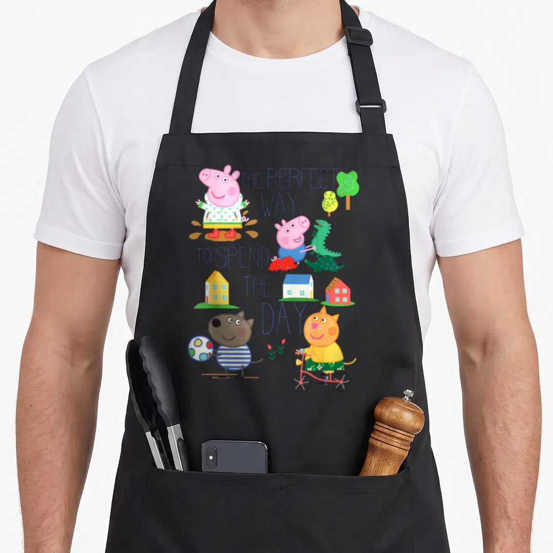 Perfect pig apron - Stacked blue text surrounded by Peppa Pig, dinosaurs, houses, and trees in pink, blue, green — shown on a black cotton canvas apron against a white background