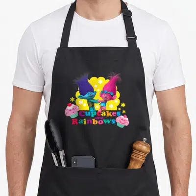 Branch cupcake apron - Two Trolls holding hands above multicolored text flanked by pink cupcakes on yellow cloud — shown on a black cotton canvas apron against a white background