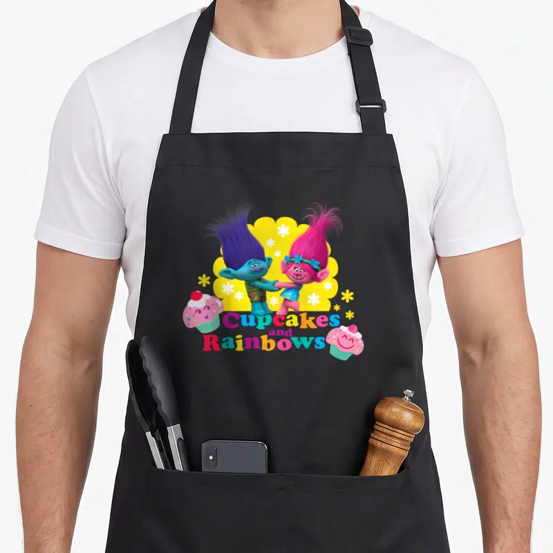 Branch cupcake apron - Two Trolls holding hands above multicolored text flanked by pink cupcakes on yellow cloud — shown on a black cotton canvas apron against a white background