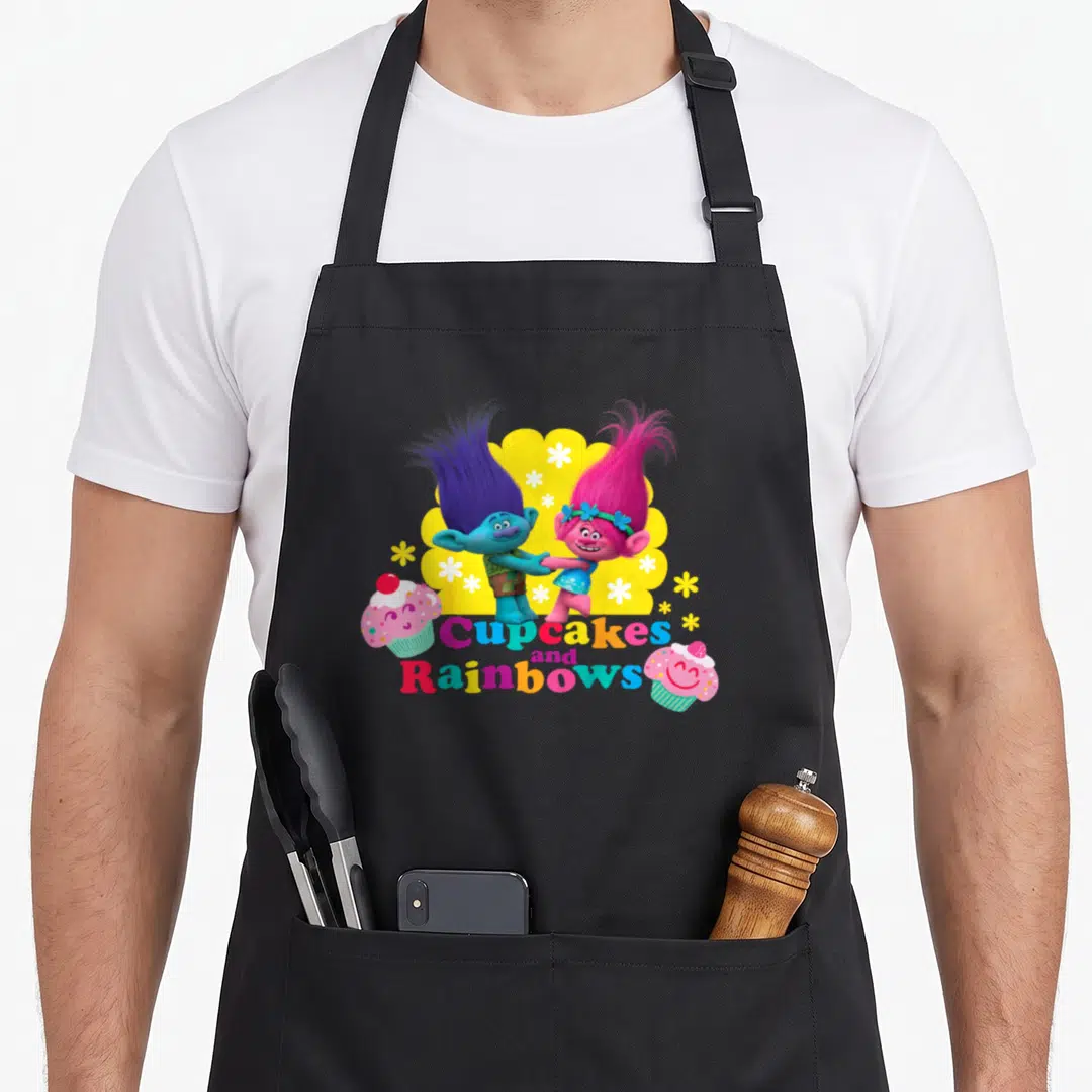 Branch cupcake apron - Two Trolls holding hands above multicolored text flanked by pink cupcakes on yellow cloud — shown on a black cotton canvas apron against a white background