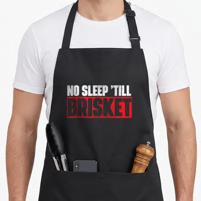 Sleep smoker apron - White text NO SLEEP 'TILL above red box containing BRISKET in grey letters — shown on a black cotton canvas apron against a white background