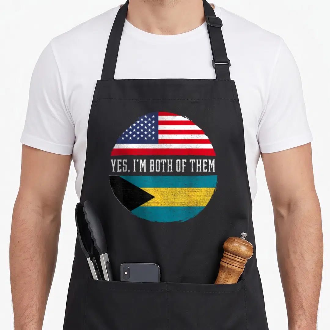 Bahamas american flag apron - Circular split design USA flag top Bahamas flag bottom white text yes im both of them — shown on a black cotton canvas apron against a white background