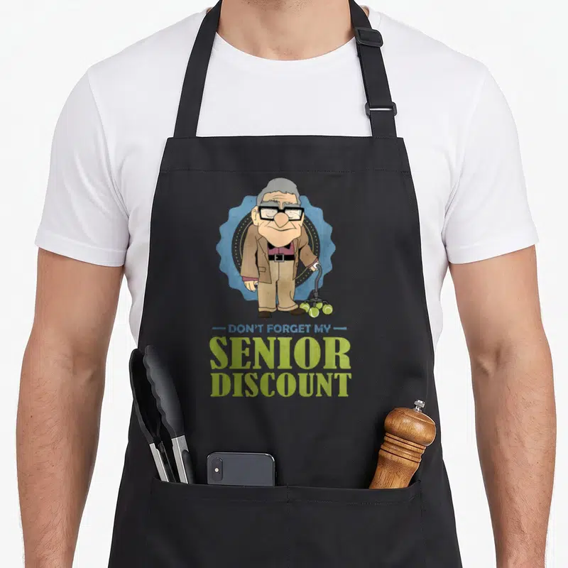 Senior discount apron - Cartoon old man with green ball walker and text Don't Forget My Senior Discount — shown on a black cotton canvas apron against a white background