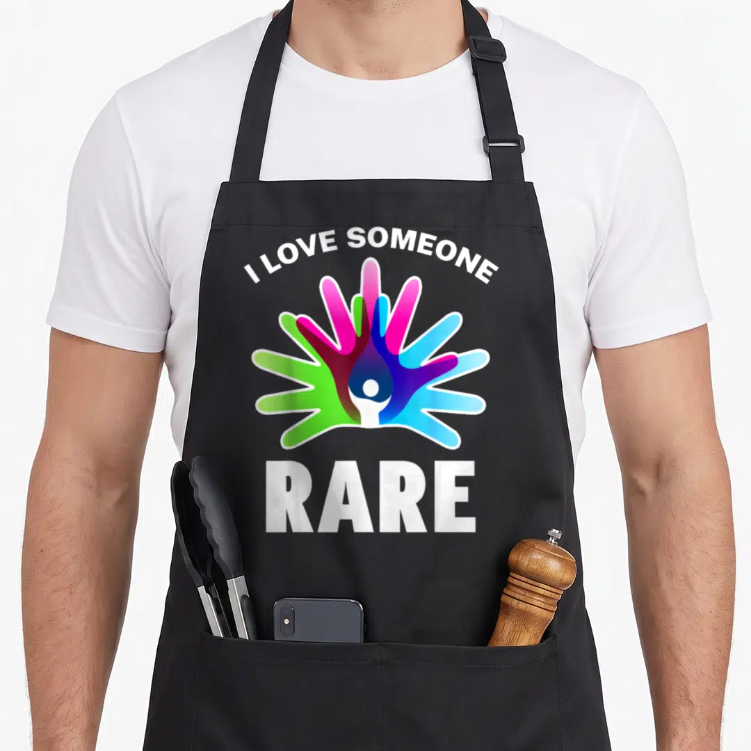 Cute rare disease awareness apron - Arched I Love Someone text above multicolored hands and RARE below — shown on a black cotton canvas apron against a white background