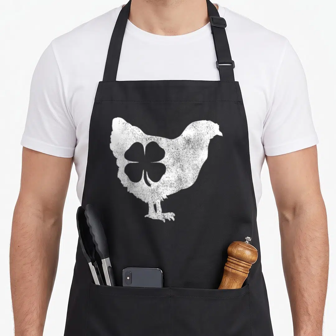Bird hen apron - Distressed white chicken silhouette with internal four-leaf clover cutout on grey background — shown on a black cotton canvas apron against a white background
