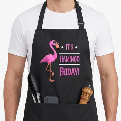 Flamingo bird apron - Pink cartoon flamingo in black sunglasses beside stacked text It's Flamingo Friday with white — shown on a black cotton canvas apron against a white background