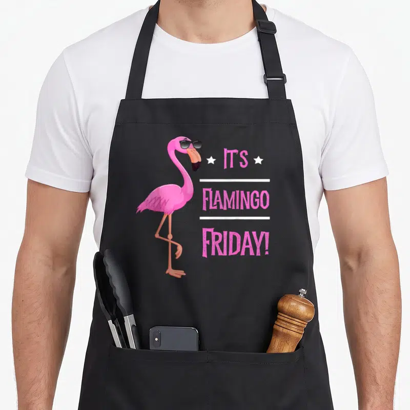Flamingo bird apron - Pink cartoon flamingo in black sunglasses beside stacked text It's Flamingo Friday with white — shown on a black cotton canvas apron against a white background