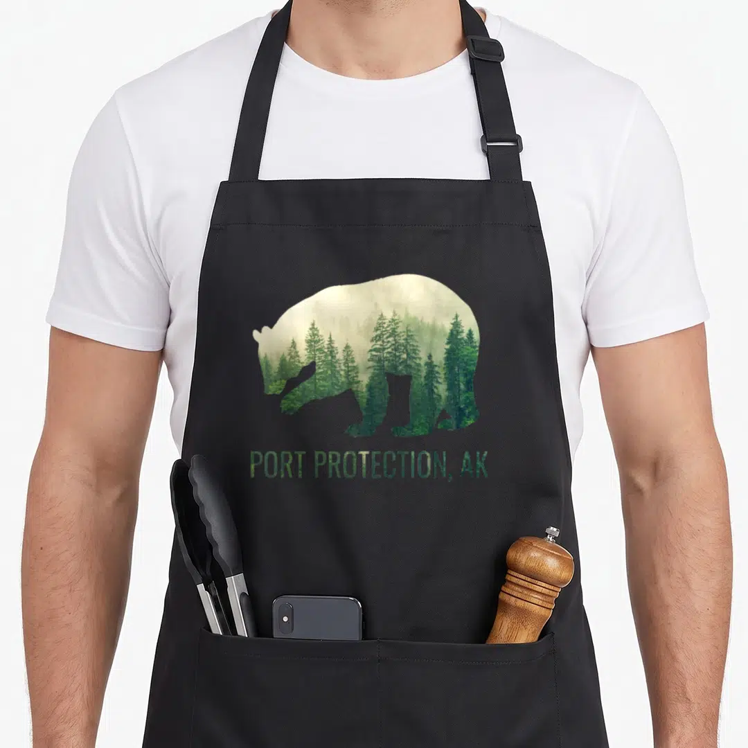 Port bear apron - Bear silhouette filled with green pine trees and fog above PORT PROTECTION, AK text — shown on a black cotton canvas apron against a white background