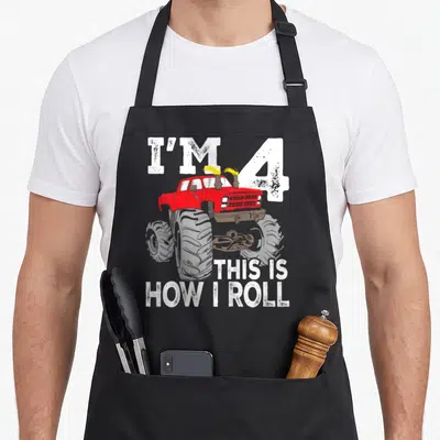 4th birthday truck apron - Red monster truck with I'M 4 and THIS IS HOW I ROLL text in white and yellow — shown on a black cotton canvas apron against a white background