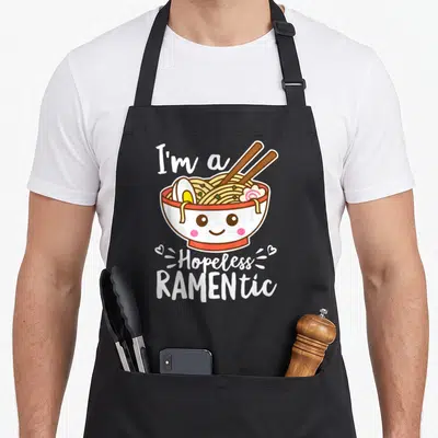 Hopeless kawaii apron - Cute kawaii ramen bowl with face and text I'm a Hopeless RAMENTic — shown on a black cotton canvas apron against a white background