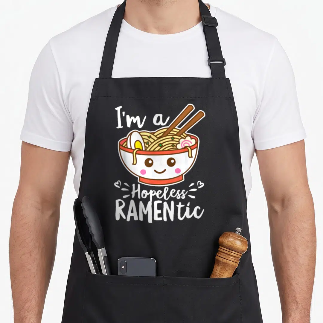 Hopeless kawaii apron - Cute kawaii ramen bowl with face and text I'm a Hopeless RAMENTic — shown on a black cotton canvas apron against a white background