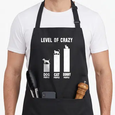 Rabbit owner bunny apron - White bar chart showing bunny people at highest level of crazy above dog and cat people — shown on a black cotton canvas apron against a white background