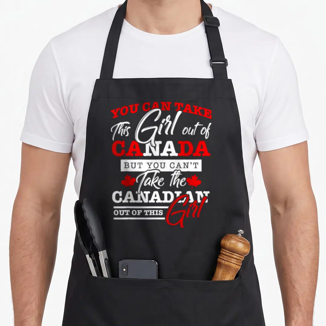 Maple leaf canadian aprons - Stacked red and white text You Can Take This Girl Out of Canada with two maple leaves — shown on a black cotton canvas apron against a white background