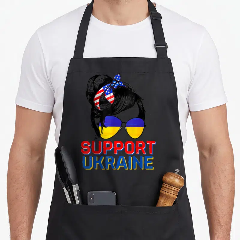 Support ukraine american flag apron - Woman silhouette with Ukrainian sunglasses and USA headband supporting Ukraine — shown on a black cotton canvas apron against a white background