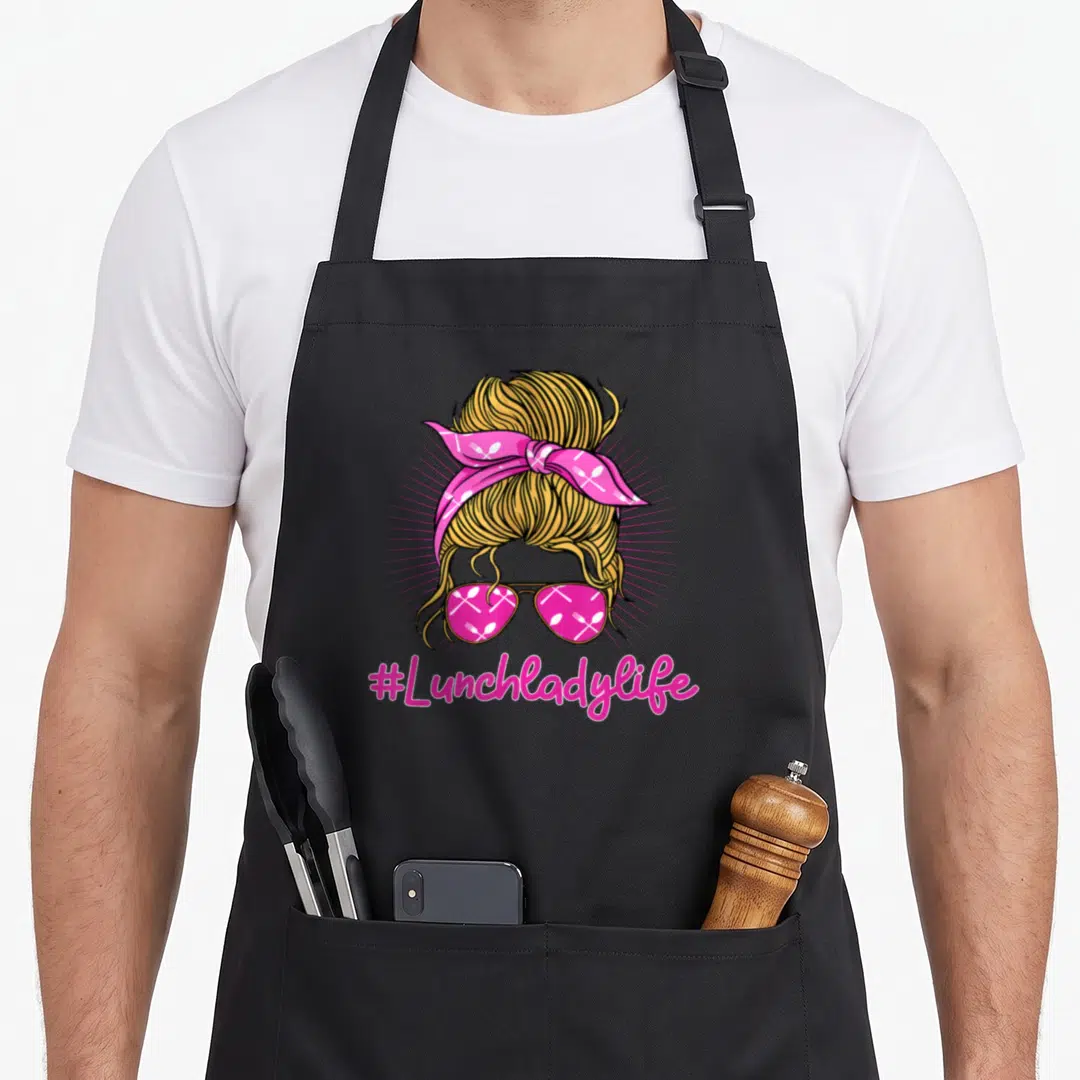 Food cafeteria aprons - Cartoon blonde woman with pink bandana and sunglasses, #Lunchladylife text below — shown on a black cotton canvas apron against a white background