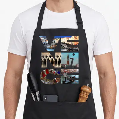 Trip italy apron - VENICE text formed by six photo collages of bridges, masks, and gondolas — shown on a black cotton canvas apron against a white background