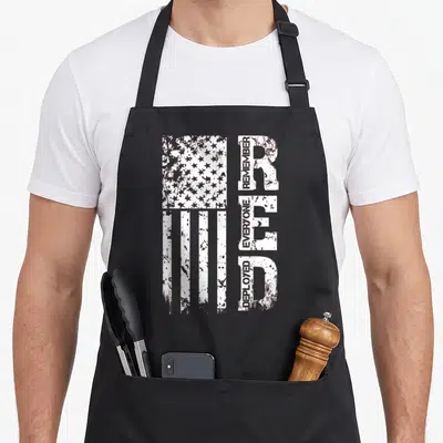 Remember air force veteran apron - White distressed USA flag next to vertical block letters containing stacked text — shown on a black cotton canvas apron against a white background