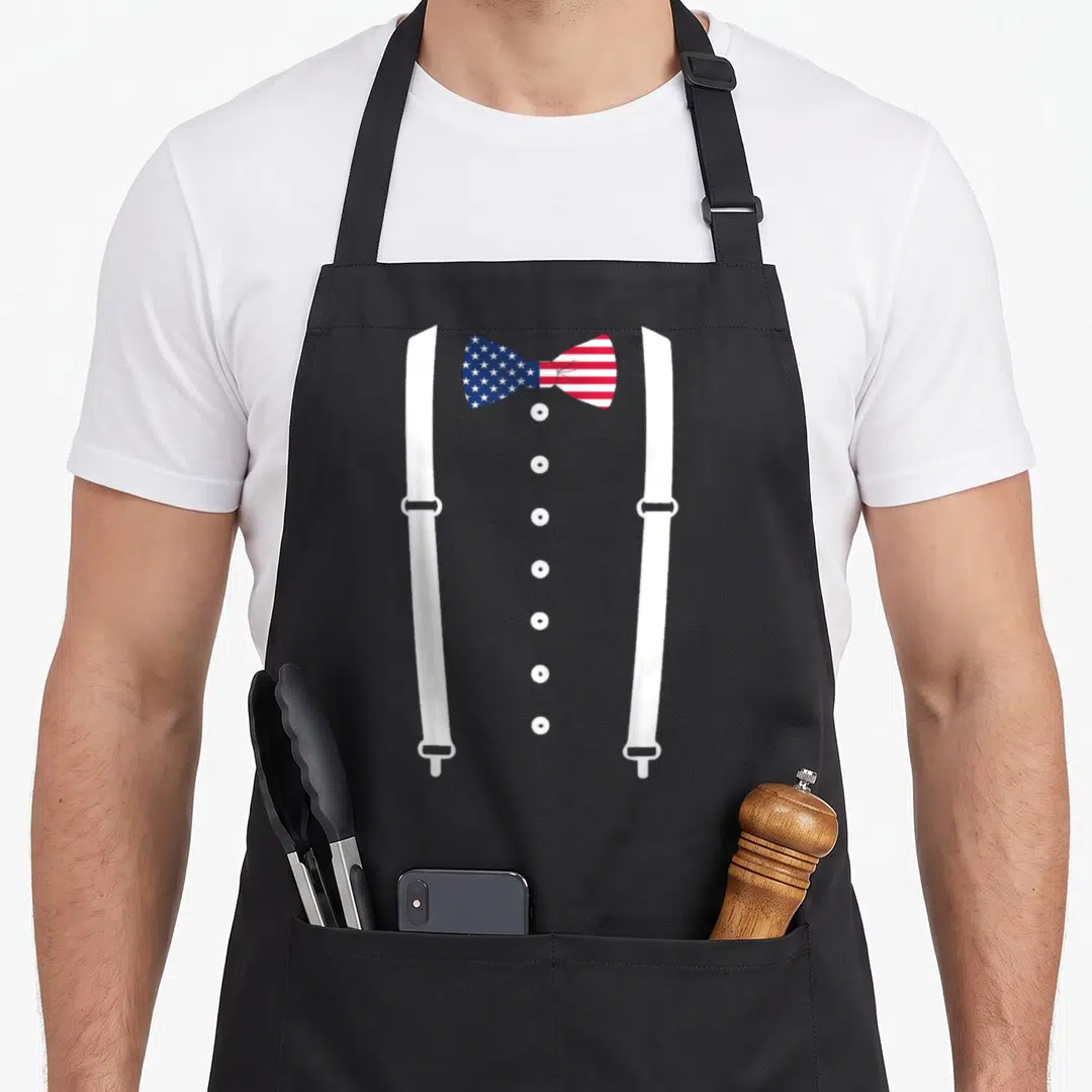 Cummerbund suspender apron - Patriotic bow tie with stars and stripes, vertical buttons, and suspenders on black apron — shown on a black cotton canvas apron against a white background
